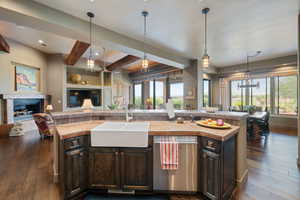 Kitchen featuring open floor plan, beamed ceiling, stainless steel dishwasher, dark brown cabinets, and dark wood-type flooring
