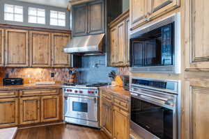 Kitchen featuring stainless steel appliances, under cabinet range hood, tasteful backsplash, and tile countertops