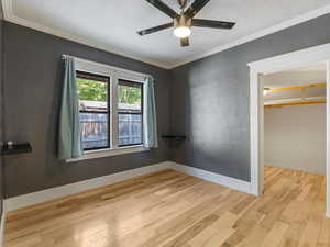 Unfurnished room with a textured ceiling, wood finished floors, crown molding, and ceiling fan