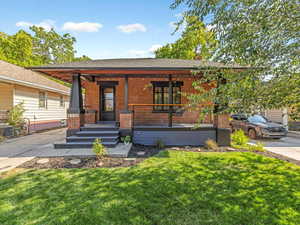 View of front facade featuring brick siding, a porch, a front lawn, and roof with shingles