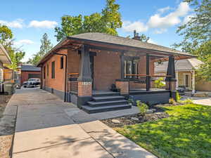 View of front of property with a porch, brick siding, driveway, a chimney, and a front lawn