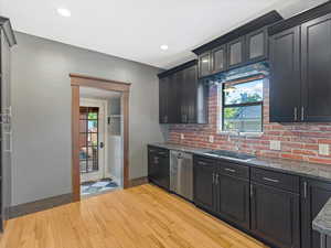 Kitchen featuring light wood-style floors, dark cabinetry, dishwasher, dark stone counters, and recessed lighting