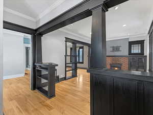 Kitchen featuring ornamental molding, wood finished floors, a fireplace, and decorative columns