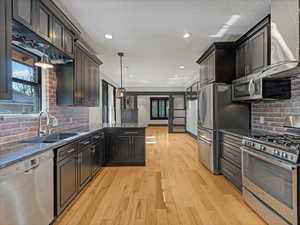 Kitchen with appliances with stainless steel finishes, light wood finished floors, recessed lighting, a textured ceiling, and backsplash