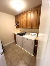 Washroom featuring cabinet space, washing machine and clothes dryer, a textured ceiling, and light tile patterned floors