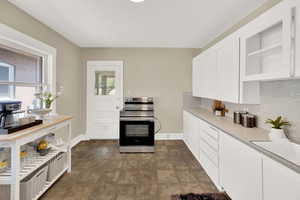Kitchen with stainless steel electric stove, white cabinets, light countertops, open shelves, and tasteful backsplash