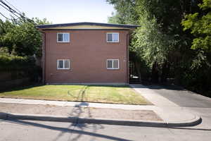 View of property exterior with brick siding, a lawn, driveway, and stairs