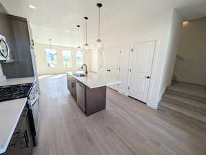 Kitchen featuring appliances with stainless steel finishes, light countertops, a center island with sink, light wood-style floors, and recessed lighting
