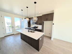 Kitchen with dark brown cabinets, light countertops, light wood finished floors, stainless steel appliances, and a center island with sink