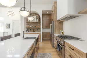 Kitchen with stainless steel appliances, light wood finished floors, light countertops, and open shelves