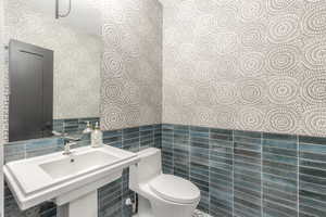 Half bath with tile walls, wallpapered walls, and a wainscoted wall