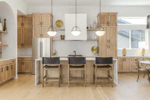 Kitchen with open shelves, light wood-style floors, freestanding refrigerator, light countertops, and a kitchen island with sink
