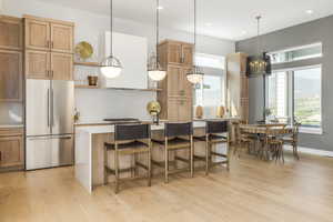 Kitchen featuring freestanding refrigerator, open shelves, light countertops, light wood-type flooring, and a breakfast bar area