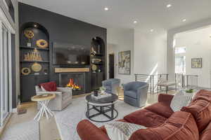 Living room featuring built in features, recessed lighting, a warm lit fireplace, and light wood finished floors