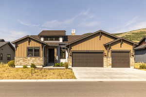Craftsman-style home with board and batten siding, stone siding, a garage, driveway, and a chimney