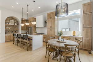 Kitchen with open shelves, light wood-style flooring, light countertops, recessed lighting, and a center island with sink