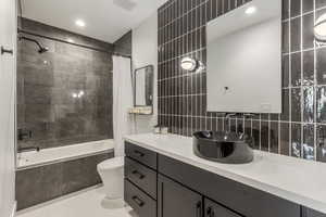 Full bath featuring tiled shower / bath combo, tile patterned flooring, vanity, tile walls, and tasteful backsplash