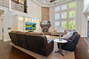 Living area with a fireplace, a towering ceiling, dark wood finished floors, and a ceiling fan