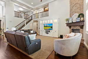 Living room featuring dark wood-style flooring, a brick fireplace, a towering ceiling, and stairway