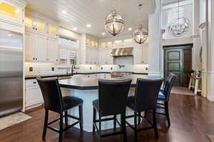 Kitchen with dark countertops, under cabinet range hood, a kitchen bar, built in fridge, and recessed lighting