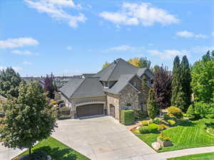 View of front of home with stone siding, a garage, driveway, a front yard, and roof with shingles