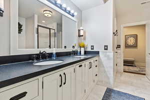 Bathroom with tile walls, double vanity, a shower stall, a wainscoted wall, and a textured ceiling