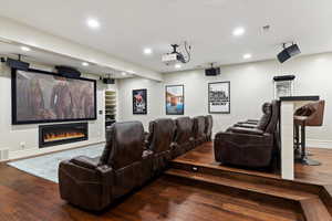 Home theater room featuring recessed lighting, a glass covered fireplace, and wood finished floors