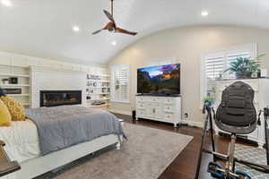 Bedroom with vaulted ceiling, recessed lighting, dark wood-type flooring, a fireplace, and a ceiling fan
