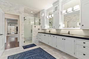 Full bath featuring a stall shower, double vanity, and decorative backsplash