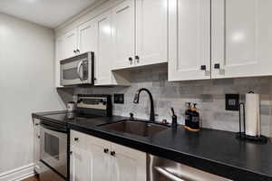 Kitchen featuring appliances with stainless steel finishes, backsplash, white cabinets, and dark countertops