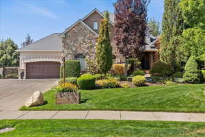 View of front of home featuring a front yard, a garage, driveway, and stone siding
