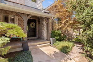 Property entrance featuring roof with shingles, brick siding, and a porch
