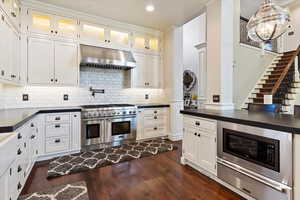 Kitchen featuring dark countertops, stainless steel appliances, under cabinet range hood, dark wood-style floors, and a warming drawer