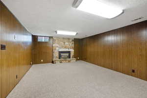 Below grade area with wood walls, carpet, a stone fireplace, and a textured ceiling