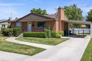 View of front of house with an attached carport, concrete driveway, brick siding, a chimney, and roof with shingles
