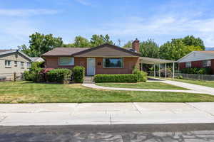 Single story home featuring concrete driveway, brick siding, a chimney, and a carport