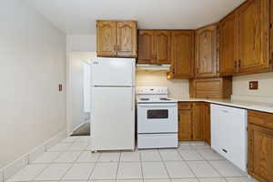 Kitchen featuring white appliances, brown cabinets, and light tile patterned floors