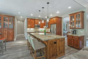 Kitchen with decorative backsplash, brown cabinetry, arched walkways, appliances with stainless steel finishes, and glass insert cabinets