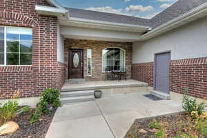 Doorway to property with a porch, a shingled roof, stucco siding, and brick siding