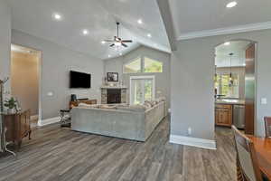 Living room with a fireplace, dark wood-style flooring, arched walkways, a ceiling fan, and recessed lighting