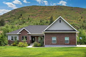 Single story home featuring a front lawn, brick siding, roof with shingles, and a mountain view
