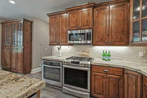 Kitchen with appliances with stainless steel finishes, backsplash, light stone countertops, dark wood-type flooring, and recessed lighting