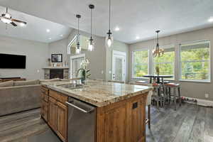 Kitchen with stainless steel dishwasher, open floor plan, brown cabinetry, a fireplace, and dark wood-style floors
