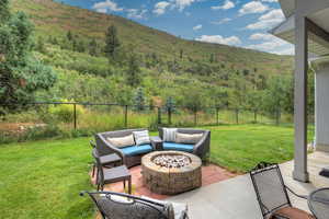 Fenced backyard featuring a fire pit, a patio area, a wooded view, and a mountain view