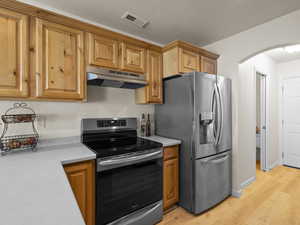 Kitchen featuring appliances with stainless steel finishes, light wood-type flooring, under cabinet range hood, and light countertops