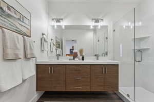 Full bathroom with double vanity, a shower stall, and wood finished floors
