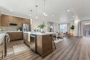 Kitchen with open floor plan, light countertops, backsplash, appliances with stainless steel finishes, and brown cabinets