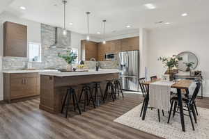 Kitchen featuring tasteful backsplash, appliances with stainless steel finishes, a kitchen breakfast bar, light countertops, and a center island with sink