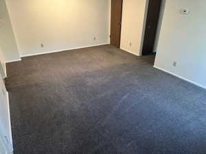 Unfurnished living room featuring dark colored carpet and baseboards
