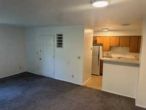 Kitchen featuring light countertops, brown cabinetry, light carpet, and freestanding refrigerator